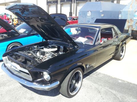 1965 Ford Mustang - A black coupe is parked with its hood open, revealing the engine bay. Another vehicle is parked nearby.
