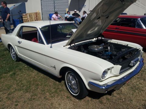 1965 Ford Mustang - A white 1965 Ford Mustang coupe is displayed with its hood open, revealing the engine bay.