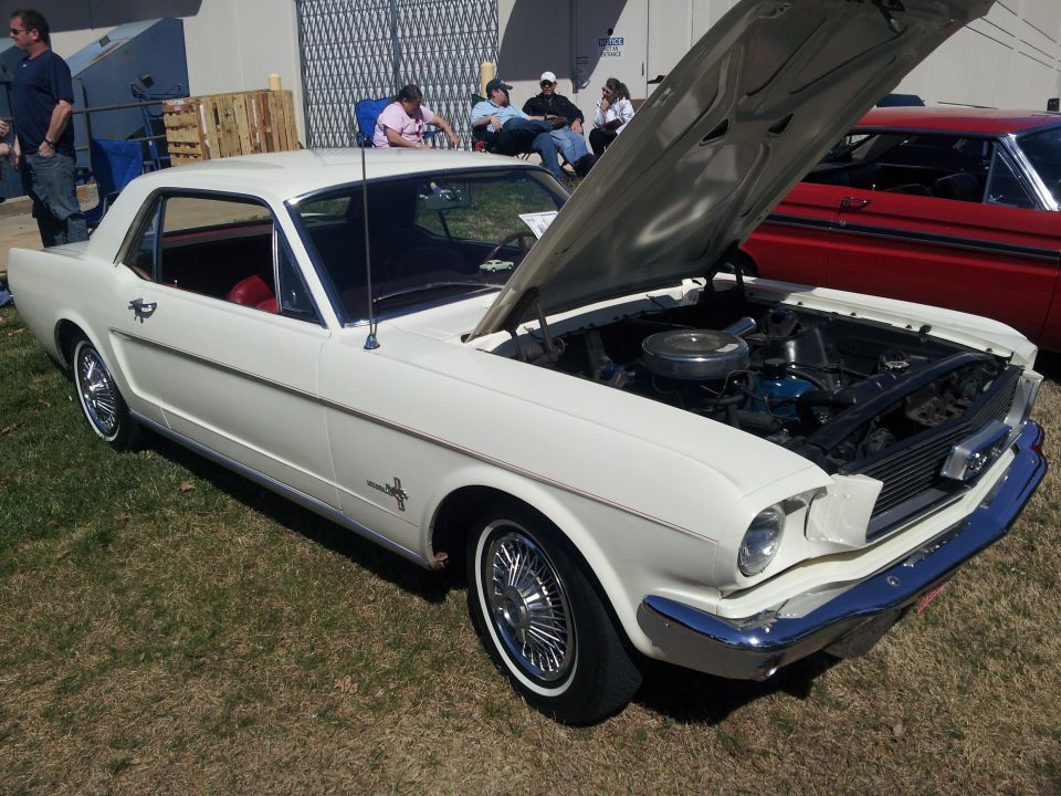 White 1965 Ford Mustang coupe with hood open, showing engine and red interior, parked on grass