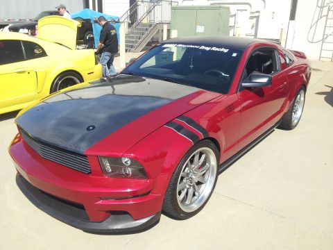 1965 Ford Mustang - A red Ford Mustang with a custom hood and racing stripes is parked next to a yellow Mustang.