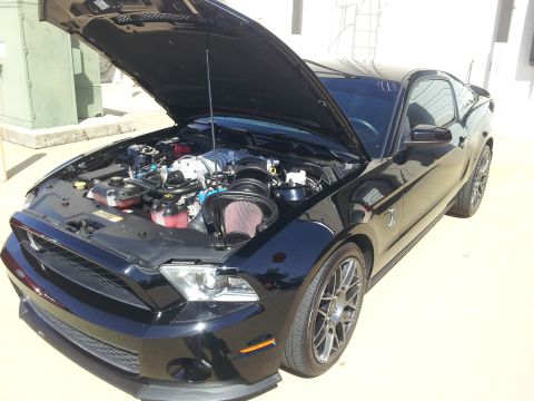 1965 Ford Mustang - Black Ford Mustang with hood open, revealing a supercharged engine with a prominent red air filter.