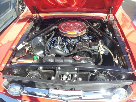 1965 Ford Mustang - Close-up of a classic red 1965 Ford Mustang's engine compartment, a chrome air filter housing.