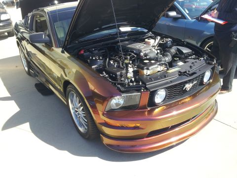 1965 Ford Mustang - This Mustang features a unique chameleon paint job and a supercharged engine, with another Mustang visible in the background.