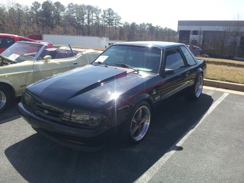 1965 Ford Mustang - This black Ford Mustang coupe, likely from the 1990s, features a distinctive hood scoop and 5.0 badging.