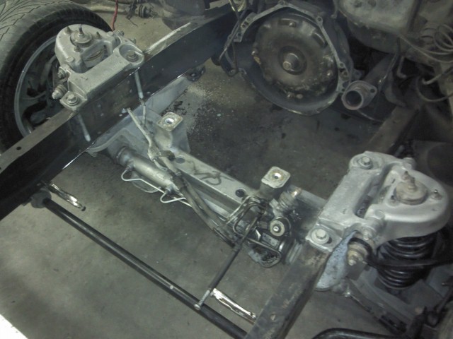 Close-up of a vehicle's frame, showing suspension components, steering rack, and part of the transmission