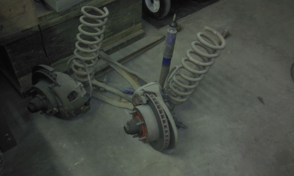 Two front suspension assemblies with coil springs and disc brakes are laid out on a concrete floor