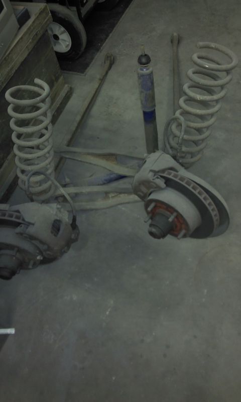 1967 Ford F-100 - Vehicle suspension components including springs, a shock, and brake assemblies are laid out on a garage floor.