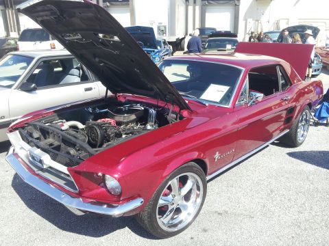 1965 Ford Mustang - A red 1967 Ford Mustang coupe is displayed with its hood open, revealing the engine and custom chrome wheels.