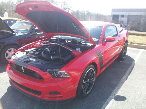 1965 Ford Mustang - Red Ford Mustang Boss 302 with hood open, parked next to another vehicle.