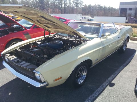 1965 Ford Mustang - A yellow convertible with its hood open is parked next to another vehicle on a sunny day.
