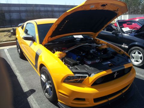 1965 Ford Mustang - A yellow 2011 Ford Mustang Boss 302 is displayed with its hood open, revealing the engine compartment. A second Mustang is parked nearby.