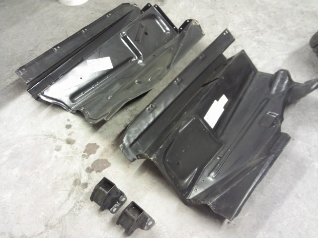 Two black metal automotive floor pan sections and two small brackets on a concrete floor