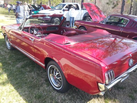 1965 Ford Mustang - A red 1965 Ford Mustang convertible is parked on grass next to other vehicles.