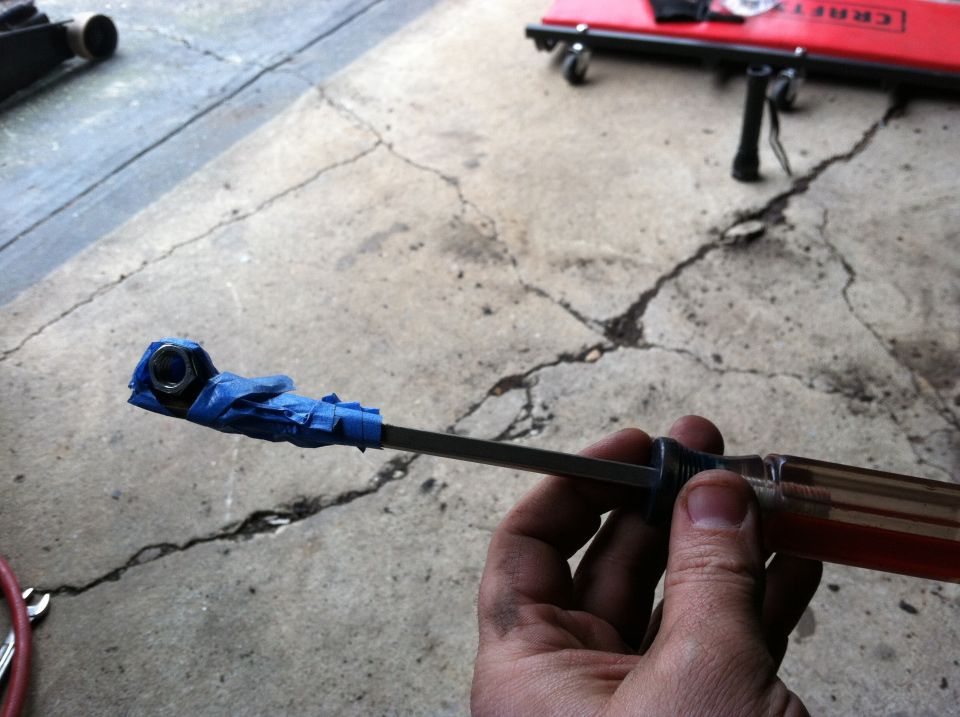 Screwdriver with blue tape wrapped around its tip, holding a nut