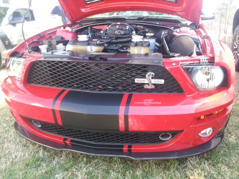1965 Ford Mustang - Front view of a red Ford Mustang Shelby Super Snake, hood open, revealing the engine and distinctive grille.