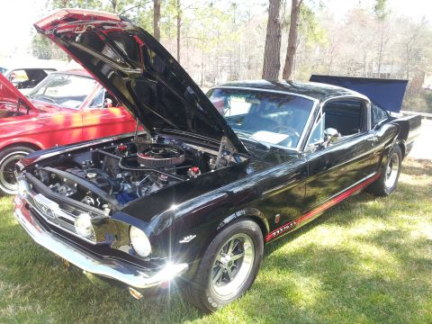 1965 Ford Mustang - A black 1965 Ford Mustang is displayed with its hood and trunk open, parked on grass.