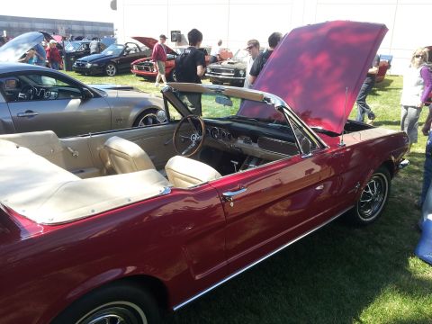 1965 Ford Mustang - A classic red convertible is displayed at an outdoor car show with its hood open.