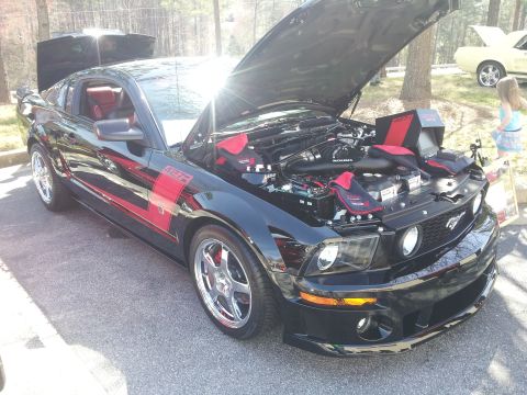 1965 Ford Mustang - Black Ford Mustang with red racing stripes and hood open, revealing the engine bay.