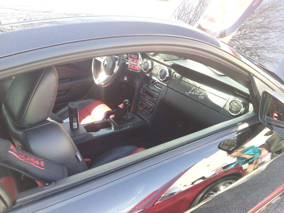 Black car interior with red accents on seats and door panels, a black spray can on the center console, and a signature on the dashboard