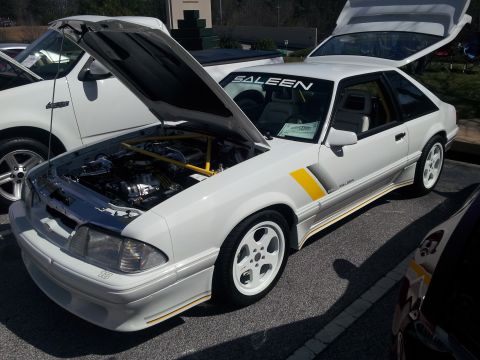 1965 Ford Mustang - A white Saleen Mustang is displayed with its hood and trunk open, parked next to a white truck.