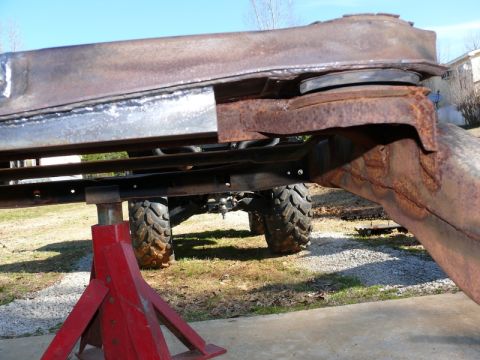 1976 Chevrolet Corvette - Close-up of a heavily rusted vehicle frame supported by red jack stands, with large off-road tires visible in the background.