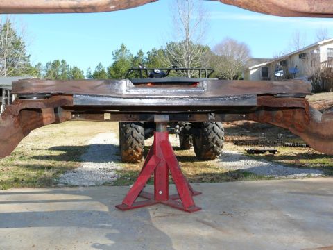 1976 Chevrolet Corvette - This rusted frame assembly is held up by red jack stands, with large tires visible behind it.