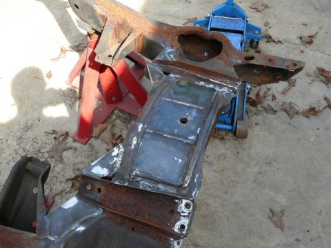 1976 Chevrolet Corvette - A heavily rusted car frame is supported by jack stands and a blue hydraulic jack on a concrete surface.
