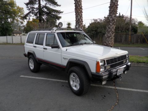 1994 Jeep Cherokee - A white 1994 Jeep Cherokee is parked in a lot, a roof rack and auxiliary lights on the roof.