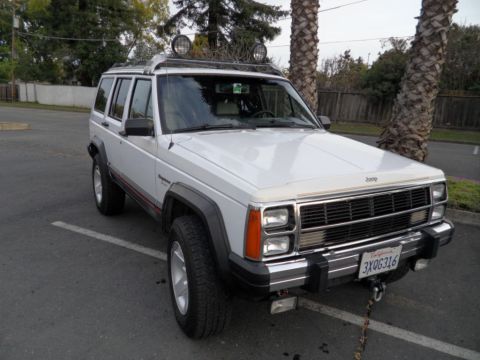 1994 Jeep Cherokee - A white Jeep Cherokee is parked in a lot, a roof rack with two auxiliary lights and a chrome grille.