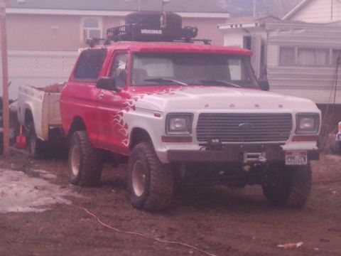 1979 Ford Bronco - A red and white pickup truck is seen from the front, equipped with a roof rack.