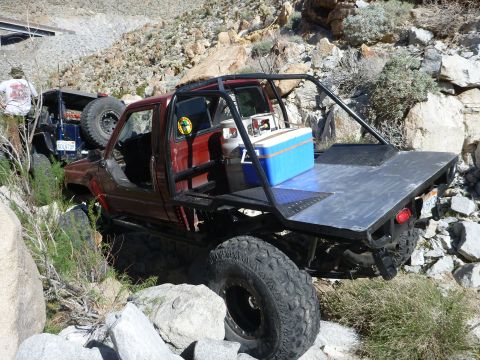 1997 Ford Ranger - A modified red pickup truck navigates a rocky, off-road trail with another vehicle behind it.