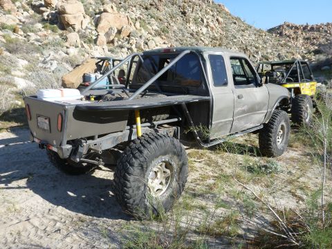 1997 Ford Ranger - This heavily modified truck features a custom flatbed and roll cage, parked in a rocky, desert landscape.