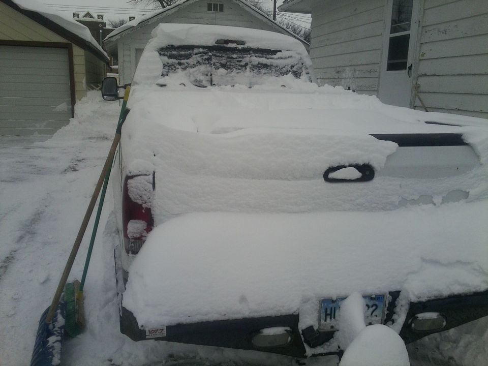 Rear view of a 2000 Ford F-250 pickup truck covered in snow, parked next to a garage