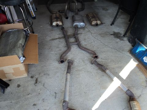 2004 Mercury Grand Marquis - Disassembled exhaust system components, including mufflers and various pipes, are arranged on a concrete surface.
