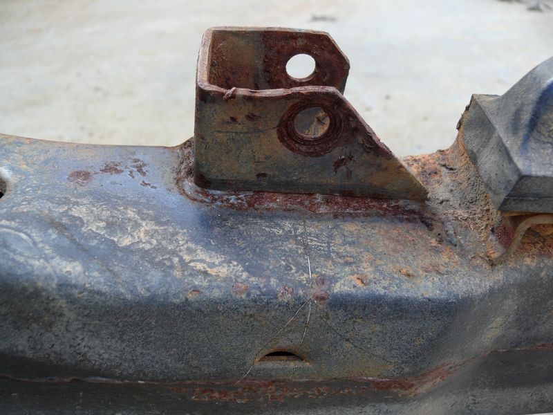 Rusted metal bracket attached to a dark, corroded frame section