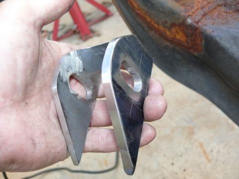 1976 Chevrolet Corvette - Two metal brackets are held in a hand, with a rusty metal surface in the background.