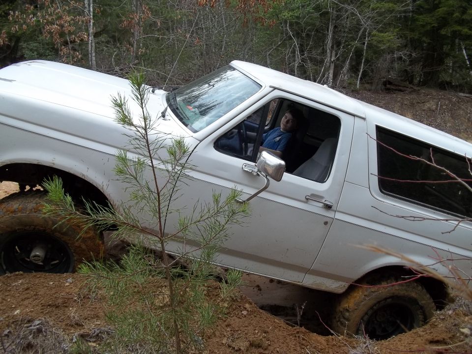 White SUV stuck in a muddy ditch with a person inside