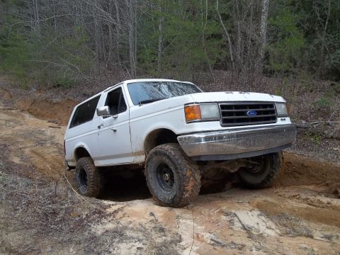 1990 Ford Bronco - This Ford Bronco is navigating a challenging off-road trail with steep inclines and loose dirt.
