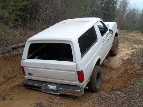 1990 Ford Bronco - White 1990 Ford Bronco navigating a challenging dirt path with visible tire tracks.