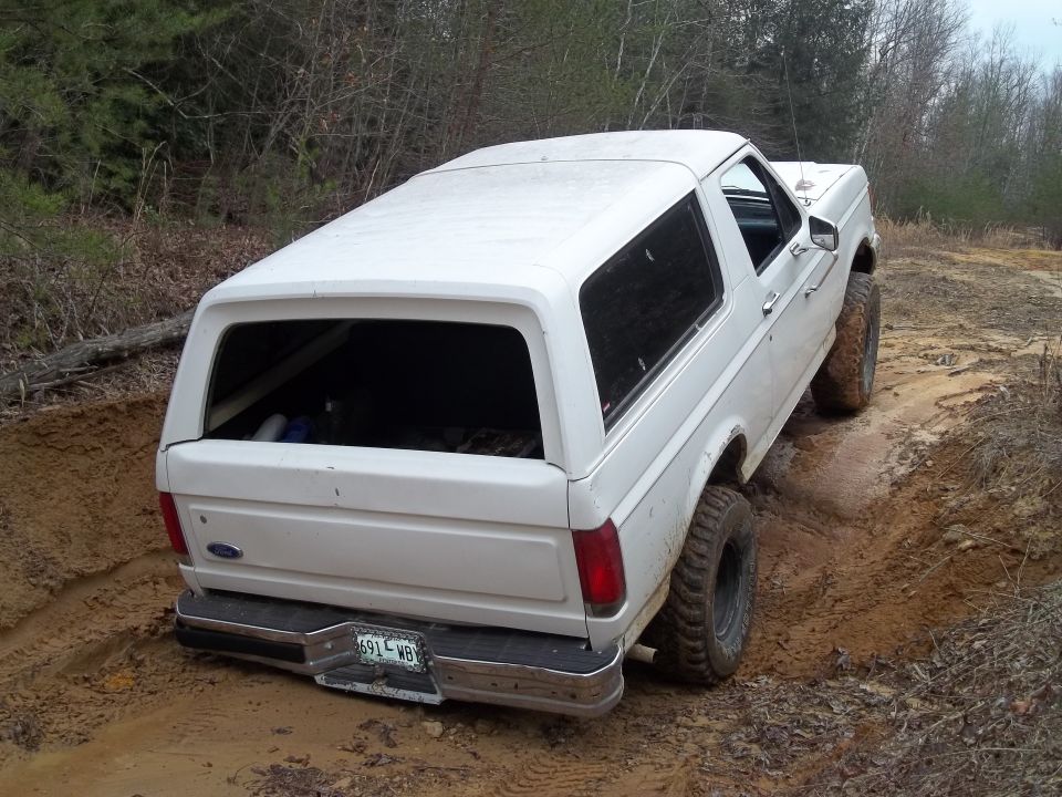 White 1990 Ford Bronco driving on a muddy trail, rear-wheel drive engaged