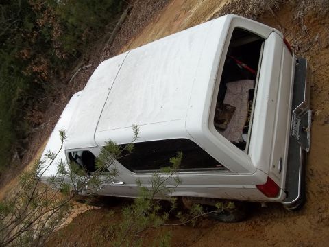 1990 Ford Bronco - A white SUV with a camper shell is stuck in the mud off-road.