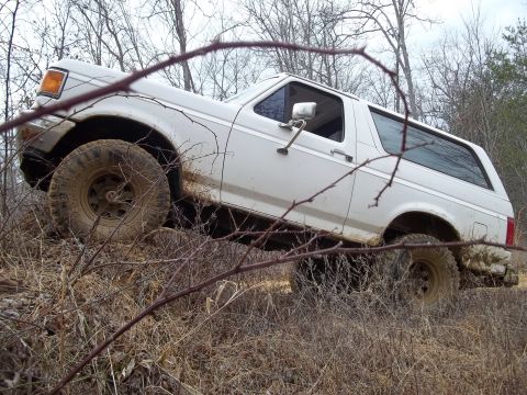 1990 Ford Bronco - A white 1990 Ford Bronco navigates a muddy, wooded trail.