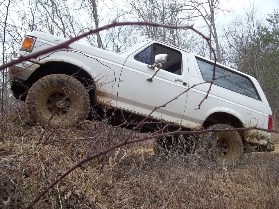 White 1990 Ford Bronco driving off-road through brush and mud