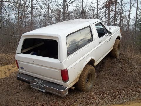 1990 Ford Bronco - White Ford Bronco navigates an off-road trail with muddy tires.
