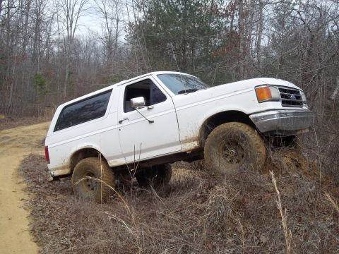 1990 Ford Bronco - This 1990 Ford Bronco navigates a challenging off-road trail with muddy tires and a tilted chassis.