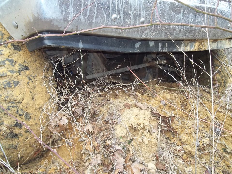 Muddy tire and undercarriage of a vehicle stuck in dirt and branches