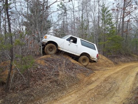1990 Ford Bronco - A white 1992 Ford Bronco navigates a steep, muddy incline on a wooded trail.