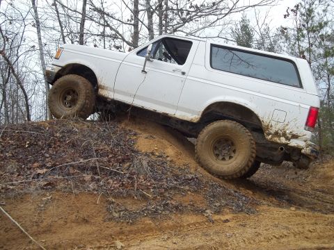 1990 Ford Bronco - White 1990 Ford Bronco tackling an off-road trail, mud splattered on its body.