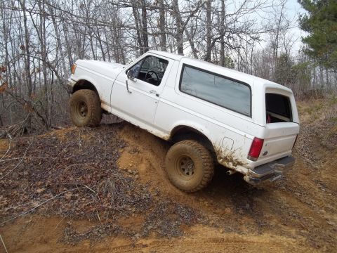 1990 Ford Bronco - This SUV is navigating a steep, muddy incline in a forest with bare trees.