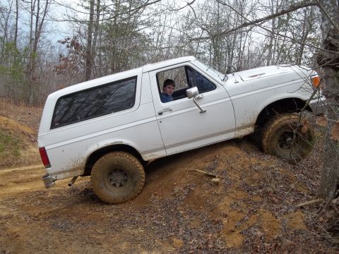 1990 Ford Bronco - A white Ford Bronco navigates a challenging off-road terrain with its driver behind the wheel.